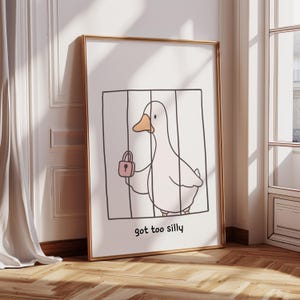 Könnte beinhalten: Gerahmter Kunstdruck mit einer Cartoon-Ente in einem Käfig, die ein rosa Vorhängeschloss hält. Die Ente hat einen gelben Schnabel und ist in einem minimalistischen Stil gezeichnet. Der Text "got too silly" steht unten.