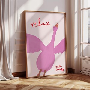 May include: A framed art print with a pink goose illustration. The word "relax" is written in red script above the goose, and "take it easy" is written in red script below. The artwork is framed in gold.