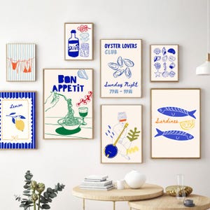 May include: A set of framed art prints with a food and leisure theme. The prints feature illustrations of food items like olives, oysters, pasta, and lemons, along with beachwear and musical instruments. The colour palette includes blue, green, and yellow on a cream background.