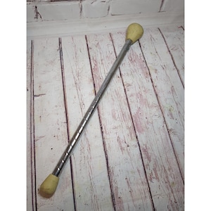 May include: A metal baton featuring a long, slender, spiraled silver-toned shaft with a smooth, rounded, off-white rubberized tip at each end. The baton is straight and cylindrical, designed for performance or rhythmic movement activities.