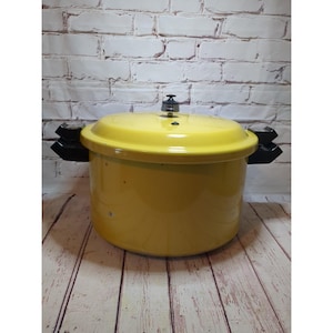 Puede incluir: Una olla a presión de color amarillo brillante con tapa a juego y dos asas laterales negras. La olla presenta un pomo metálico central en la tapa y un cuerpo cilíndrico. El diseño incluye un acabado liso y un mecanismo de cierre seguro.