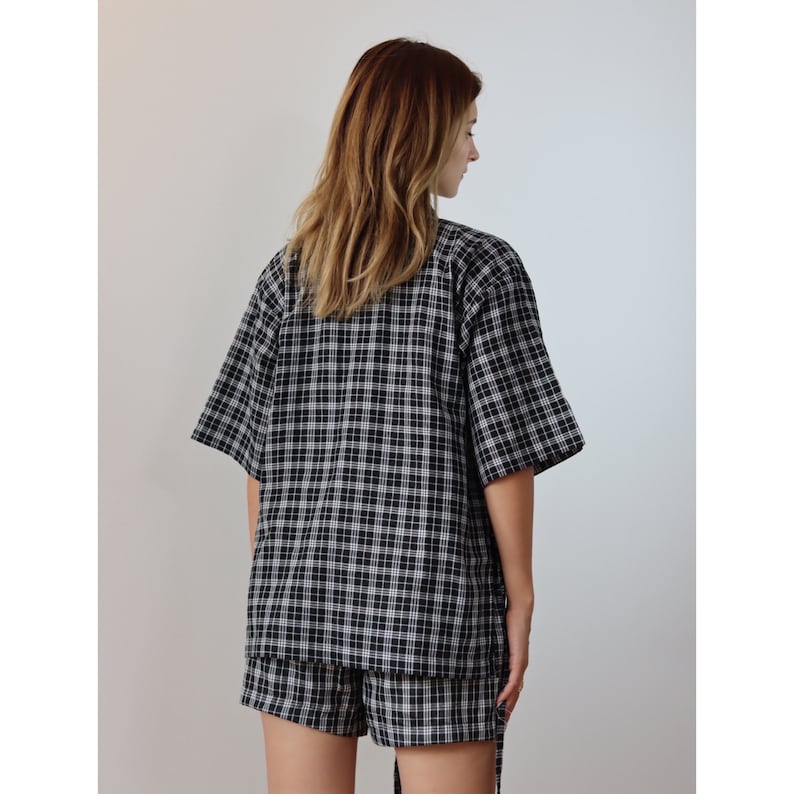 May include: A black and white plaid short-sleeved shirt and matching shorts set. The shirt has a relaxed fit and a collar. The shorts have a tie at the waist.