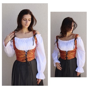 Pu&ograve; includere: Un corpetto in broccato rosso e oro con lacci e bretelle neri. Il corpetto &egrave; indossato sopra una blusa contadina bianca e una gonna nera.