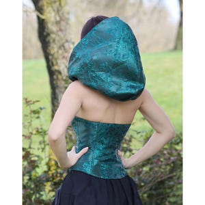 May include: A teal green hooded top with a lace pattern. The hood is large and gathered at the top. The top is made of a shiny fabric.