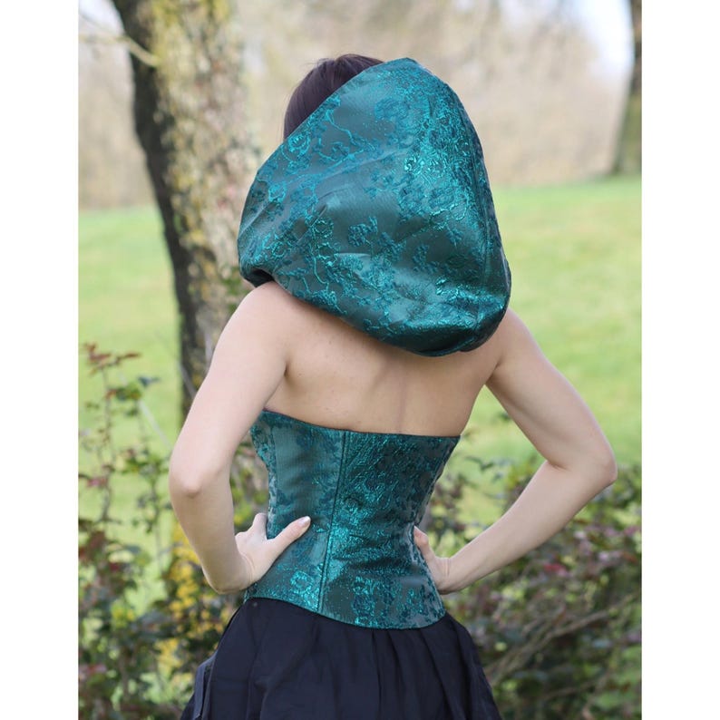May include: A teal green hooded top with a lace pattern. The hood is large and gathered at the top. The top is made of a shiny fabric.