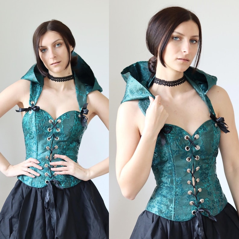 May include: A teal green corset with black lace-up detailing and a matching hooded top. The corset has a sweetheart neckline and is adorned with black ribbon bows.