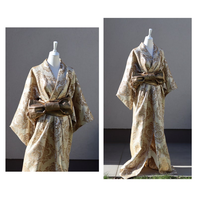 K&ouml;nnte beinhalten: Ein Kimono aus goldenem Brokat mit einer gro&szlig;en goldenen Schleife in der Taille. Der Kimono befindet sich auf einem wei&szlig;en Mannequin vor einem grauen Hintergrund.