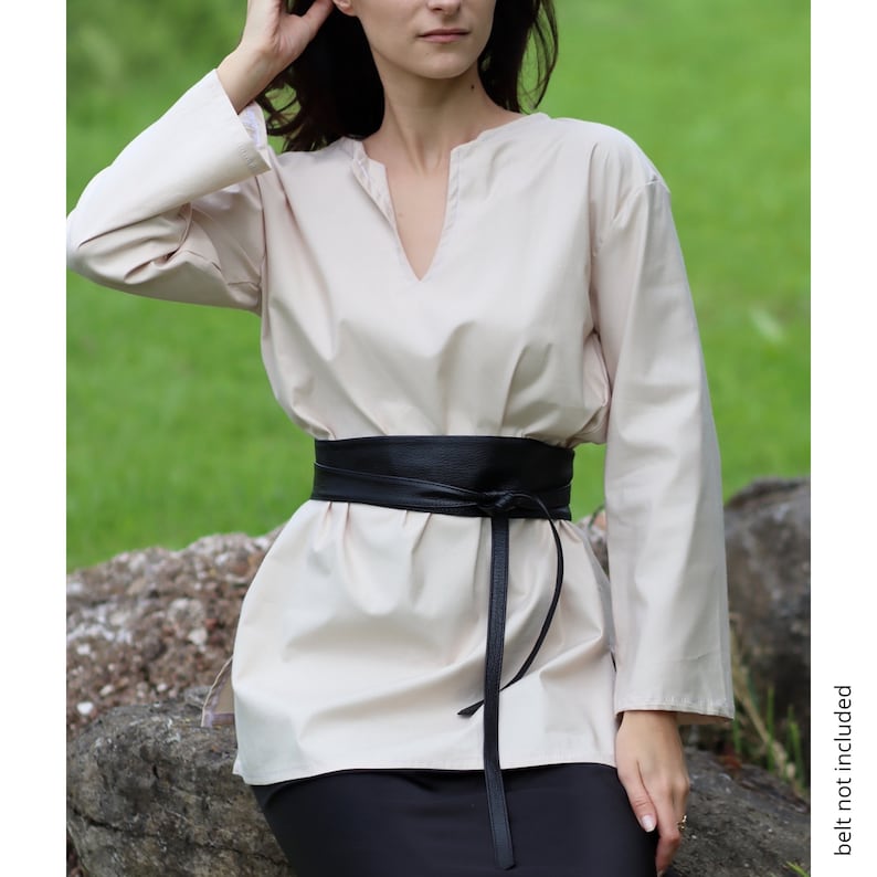 May include: A cream-colored, long-sleeved shirt with a V-neckline and a black leather belt tied at the waist.