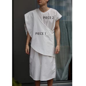May include: A white, two-piece garment set. Piece 1 is a wrap-style top, and Piece 2 is a short-sleeved top. The outfit is made of a lightweight fabric. The text "PIECE 1" and "PIECE 2" are visible on the garment.
