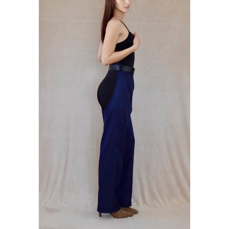 May include: A black bodysuit with a wide, navy blue overlay. The outfit is cinched at the waist with a black belt. The model is wearing brown shoes.