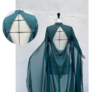 May include: A teal blue sheer cape with a low back and a fitted bodice. The cape is made of a lightweight fabric and has a flowing silhouette.