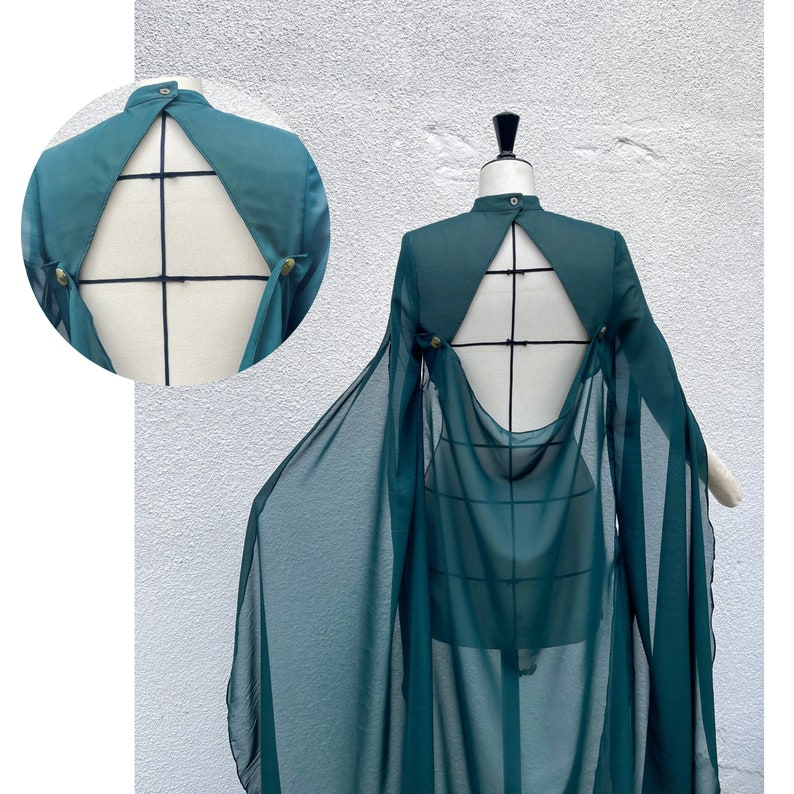 May include: A teal blue sheer cape with a low back and a fitted bodice. The cape is made of a lightweight fabric and has a flowing silhouette.