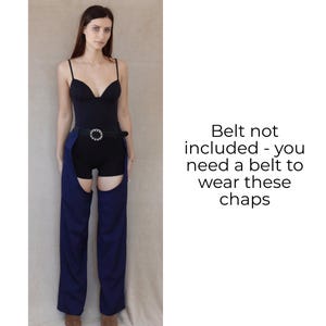 May include: A woman wearing a black bodysuit and shorts with blue chaps. The chaps have a cutout design and are worn with a belt. The text on the right says, "Belt not included - you need a belt to wear these chaps."