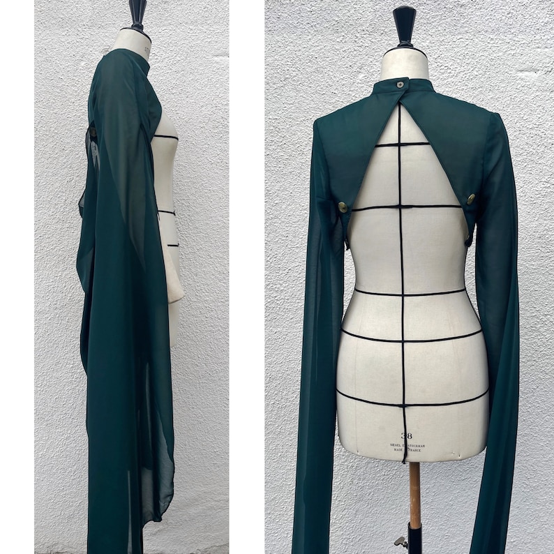 May include: A deep green sheer fabric top with long sleeves and a keyhole back. The top is on a dress form.