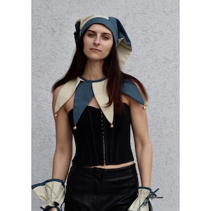 May include: A black corset with a matching jester collar and hat. The collar and hat are two-toned, with blue and cream-colored panels. The jester collar has small gold bells attached. The outfit includes matching wrist cuffs.