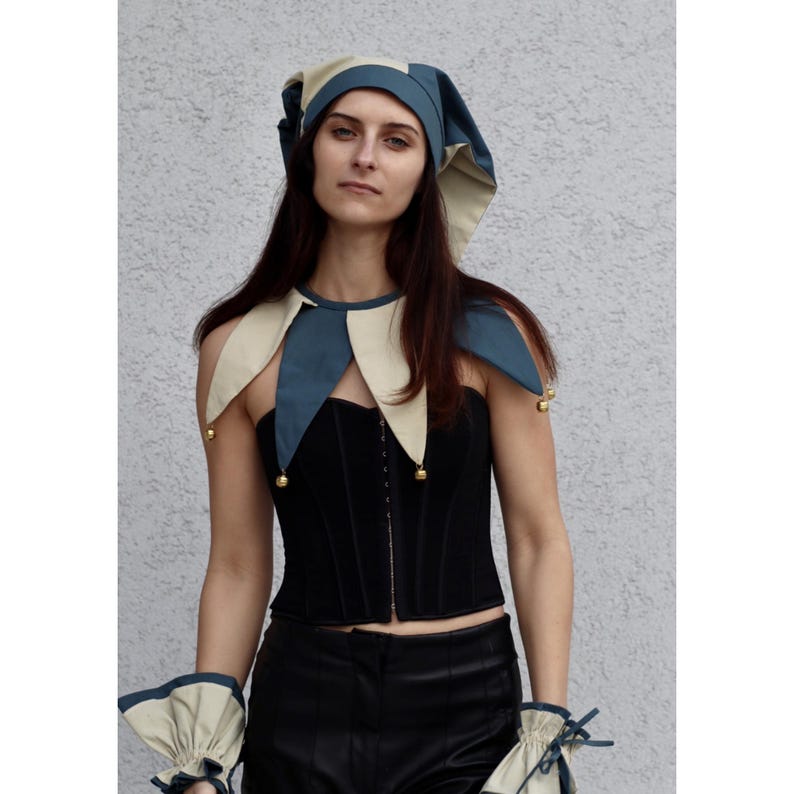 May include: A black corset with a matching jester collar and hat. The collar and hat are two-toned, with blue and cream-colored panels. The jester collar has small gold bells attached. The outfit includes matching wrist cuffs.