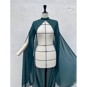 May include: A long, dark green sheer cape with a high neckline and long sleeves. The cape is open at the front and has a flowing, dramatic silhouette.
