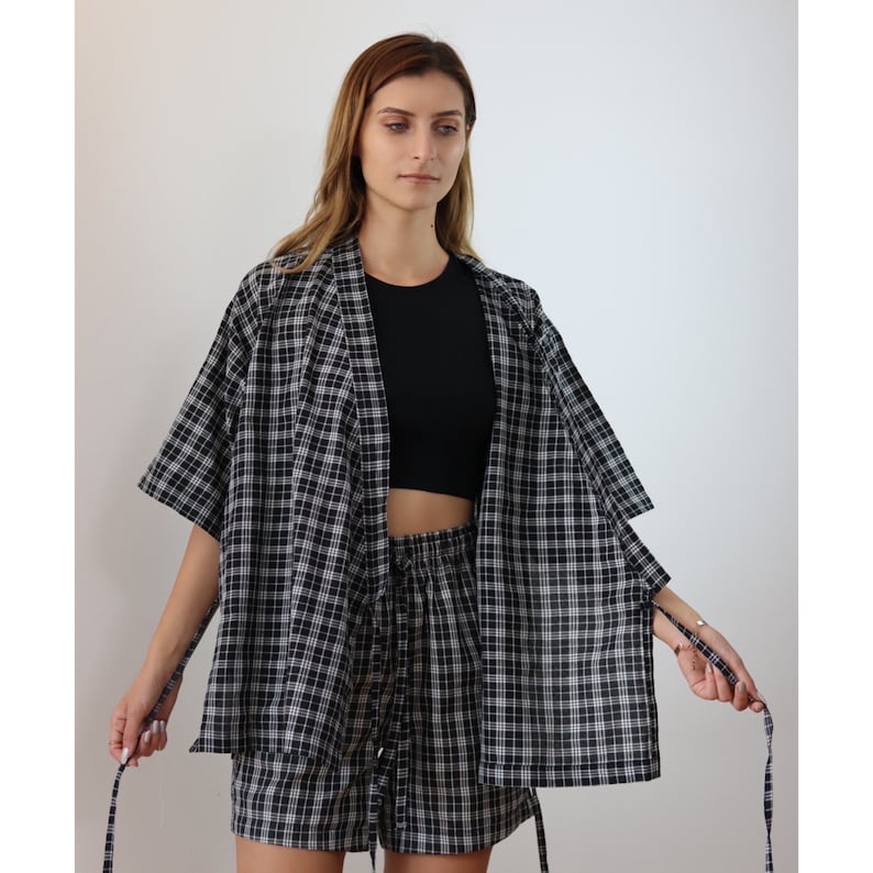 May include: A black and white plaid short-sleeved shirt and matching shorts set. The shirt has a relaxed fit and a tie at the waist. The shorts have an elastic waistband.