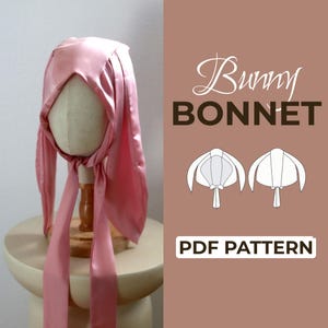 Peut inclure: Un bonnet en satin rose avec de longs panneaux latéraux en forme d'oreilles et des liens à nouer. L'image inclut le texte Bunny BONNET PDF PATTERN et deux illustrations au trait montrant les vues avant et arrière du modèle sur fond brun.