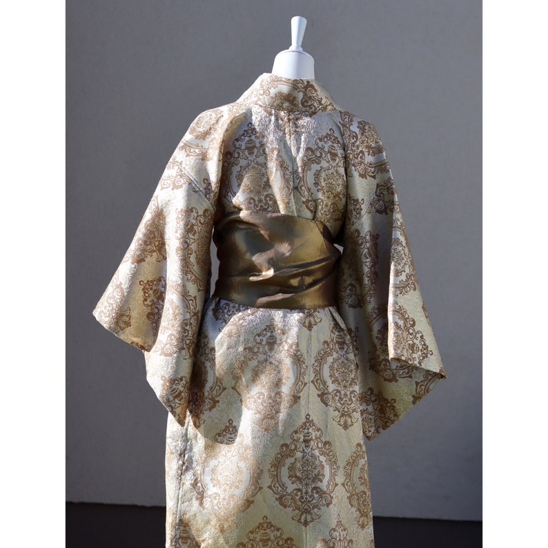 K&ouml;nnte beinhalten: Ein gold- und wei&szlig; gemustertes Kimono mit einem goldenen G&uuml;rtel. Das Kimono hat ein traditionelles japanisches Design.