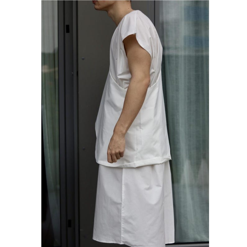 May include: A white, minimalist outfit consisting of a short-sleeved top and a knee-length skirt. The top has a unique draped design, and the skirt has a simple, clean cut. The outfit is made of a lightweight fabric, perfect for warm weather.