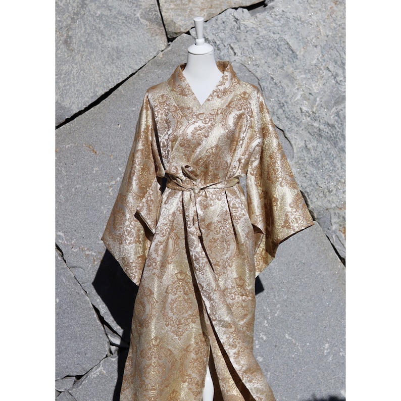 K&ouml;nnte beinhalten: Eine goldene Brokatrobe mit Paisley-Muster. Die Robe hat lange &Auml;rmel und einen Bindeg&uuml;rtel in der Taille.