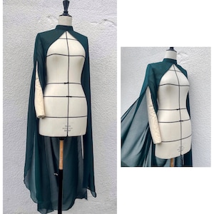 May include: A dark green sheer cape with a high neckline and a keyhole opening at the back. The cape is draped over a dress form.