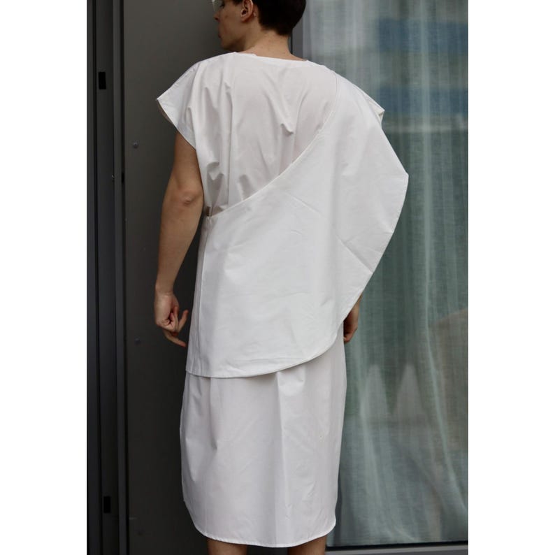 May include: A white, sleeveless tunic and draped garment. The outfit appears to be made of a lightweight fabric. The model is wearing a white tunic and a draped piece of fabric over the shoulder.