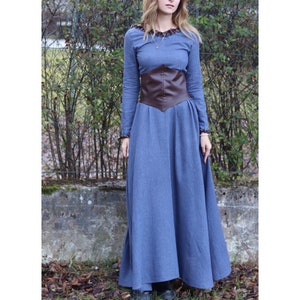 May include: A long, blue dress with a brown leather belt. The dress has a ruffled neckline and long sleeves.