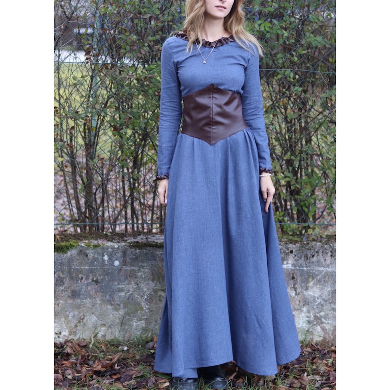 May include: A long, blue dress with a brown leather belt. The dress has a ruffled neckline and long sleeves.