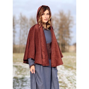 May include: A burgundy hooded cape with a long, flowing design. The cape is made of a soft, silky fabric and has a simple, elegant style.