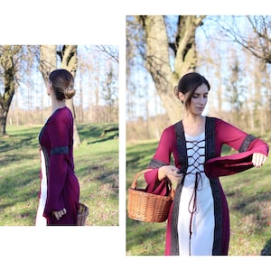 May include: A woman wearing a burgundy dress with a white lace bodice and black lace trim. The dress has long sleeves and a fitted waist. She is holding a wicker basket in her right hand. The dress has a lace-up front.