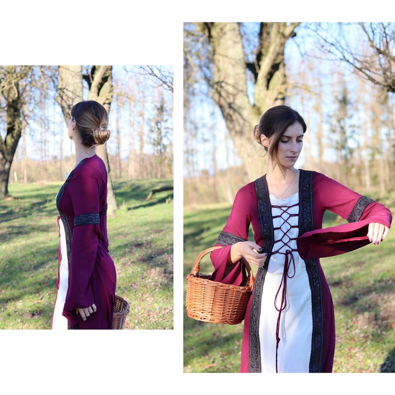 May include: A woman wearing a burgundy dress with a white lace bodice and black lace trim. The dress has long sleeves and a fitted waist. She is holding a wicker basket in her right hand. The dress has a lace-up front.