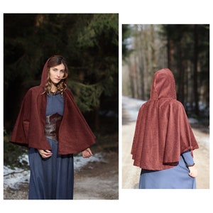 May include: A maroon hooded cape with a textured fabric. The cape is worn over a blue dress and a brown leather corset.