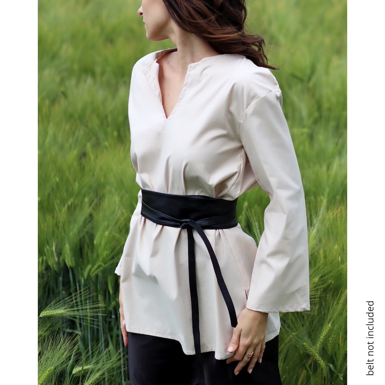 May include: A cream colored, long-sleeved shirt with a v-neck and a black leather belt tied at the waist.