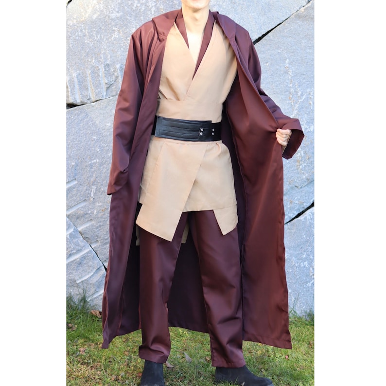 May include: A brown hooded robe with a tan under tunic and matching pants. The robe is open in the front, revealing the undergarments. A black belt with a silver buckle is worn around the waist.
