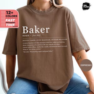 Op de afbeelding: Espresso-kleurig T-shirt met het woord "Baker" in het wit, samen met een definitie. De definitie bevat zinnen als "Dough Tamer" en "Butter Believer". Het shirt bevat ook tekst over bakken en een verwijzing naar "Powered by sugar and good vibes."