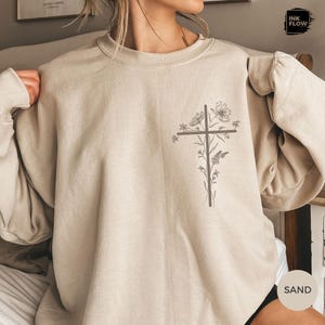 May include: Sand-coloured sweatshirt with a cross design and floral and butterfly accents. The graphic is printed on the front of the long-sleeved, crew neck top. The sweatshirt has a relaxed fit.