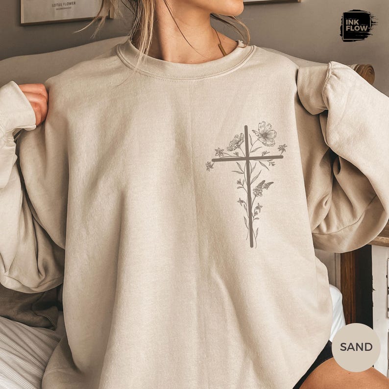 May include: Sand-coloured sweatshirt with a cross design and floral and butterfly accents. The graphic is printed on the front of the long-sleeved, crew neck top. The sweatshirt has a relaxed fit.