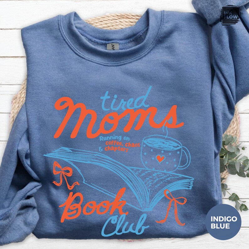 May include: Indigo blue sweatshirt with the text "tired Moms Book Club" in orange and blue. The design includes an open book, a coffee cup with a heart, and the phrase "Running on coffee, chaos & chapters."