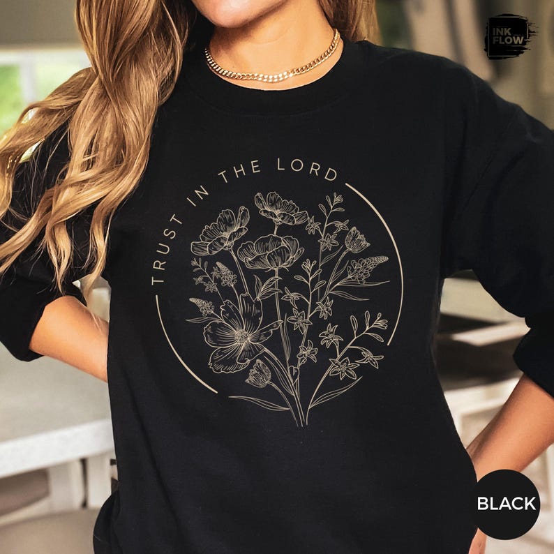 May include: Black sweatshirt with a floral design inside a circle. The words "TRUST IN THE LORD" are printed around the circle. The floral design is in a neutral color, and the sweatshirt is black.