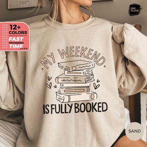 May include: A beige sweatshirt with the text "My Weekend is Fully Booked" and a stack of books with hearts around them.