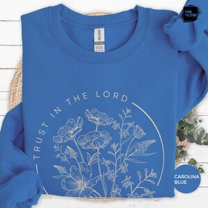 May include: Carolina blue sweatshirt with the text "TRUST IN THE LORD" in a semi-circle around a floral design. The floral design is in a light beige color. The sweatshirt is a heavy blend.