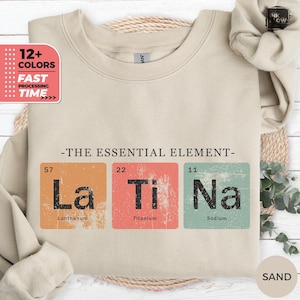 May include: Sand-colored sweatshirt with the phrase "-THE ESSENTIAL ELEMENT-" and the periodic table elements La, Ti, and Na. The sweatshirt also has a graphic that says "12+ COLORS" and "FAST PROCESSING TIME."