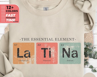 May include: Sand-colored sweatshirt with the phrase "-THE ESSENTIAL ELEMENT-" and the periodic table elements La, Ti, and Na. The sweatshirt also has a graphic that says "12+ COLORS" and "FAST PROCESSING TIME."