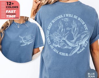 May include: Blue jean-coloured t-shirt with a whale and aquatic plants design. The back has a circular graphic with the text "WHEN YOU GO THROUGH DEEP WATERS, I WILL BE WITH YOU Isaiah 43:2". The front has a smaller whale graphic.