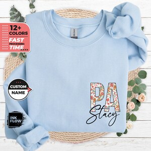 May include: Light blue sweatshirt with a floral patterned "PA Stacy" design. The sweatshirt is a blank canvas for customization with a custom name option.