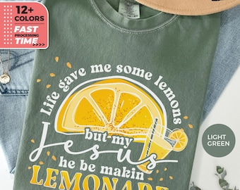 Może przedstawiać: Jasnozielona koszulka z napisem "Life gave me some lemons but my Jesus he be makin LEMONADE" oraz grafiką plasterka cytryny i szklanki lemoniady. Koszulka ma również napis "12+ COLORS" i "FAST PROCESSING TIME".