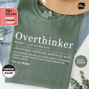 May include: A light green t-shirt with the word "Overthinker" in white, along with a definition. The shirt also features the text "ANALYTICAL, RESTLESS, MENTALLY BUSY" and "See also: Kate". A "Custom Name" button is visible.