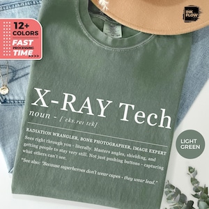 Könnte beinhalten: Hellgrünes X-Ray Tech T-Shirt mit weißem Text. Das Shirt enthält eine Definition von X-Ray Tech, die ihre Rolle als Strahlungswrangler und Bildexperte beschreibt. Das Shirt hat auch eine Grafik mit der Aufschrift "12+ COLORS" und "FAST PROCESSING TIME".